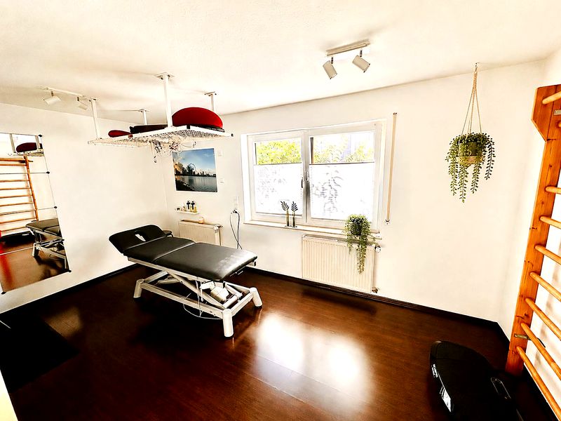 Behandlungszimmer mit Therapieliege, Sprossenwand und hellen Pflanzen am Fenster