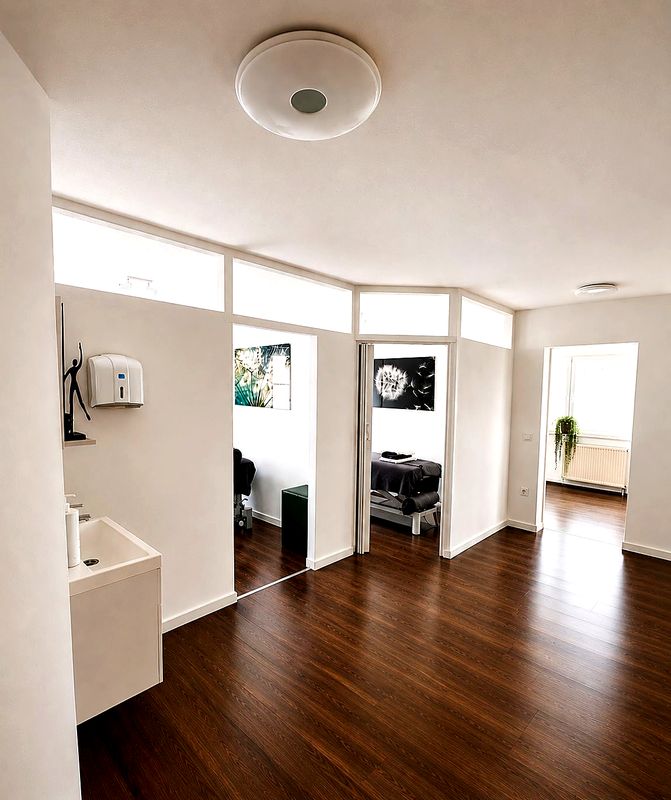 Heller Flur mit Blick in die Behandlungszimmer, Waschbecken und Holzboden